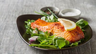A bowl of green leafy salad with a grilled salmon on it