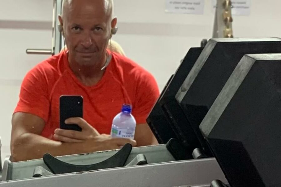 Mark leaning on gym equipment wearing an orange t-shirt