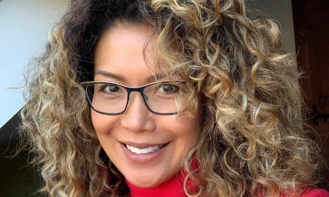 Woman with curly hair and glasses smiling at the camera