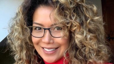Woman with curly hair and glasses smiling at the camera