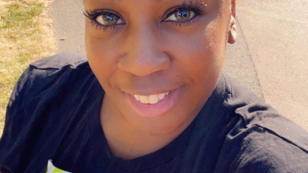 A woman close to the camera smiling, wearing a running number